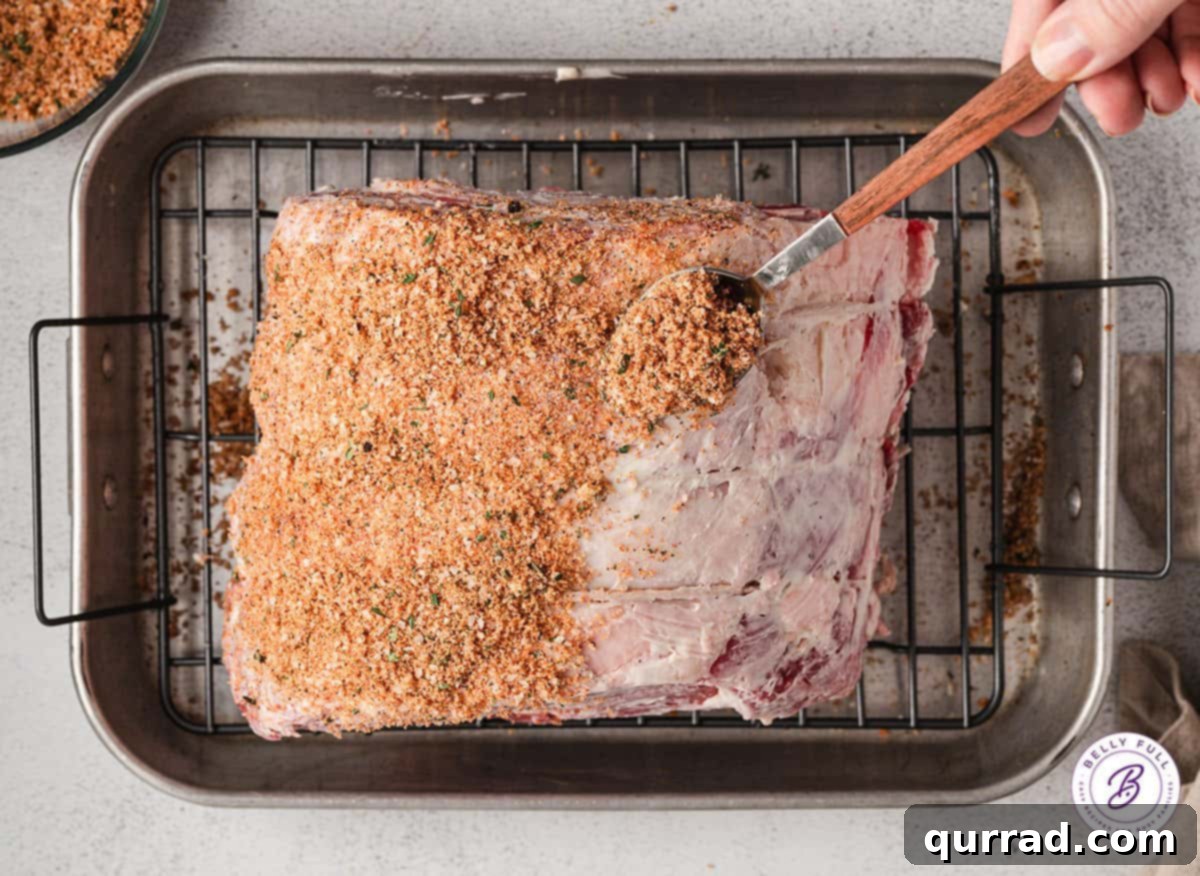 A prime rib roast is shown with the homemade rub being generously applied to its surface, illustrating the correct technique for seasoning.
