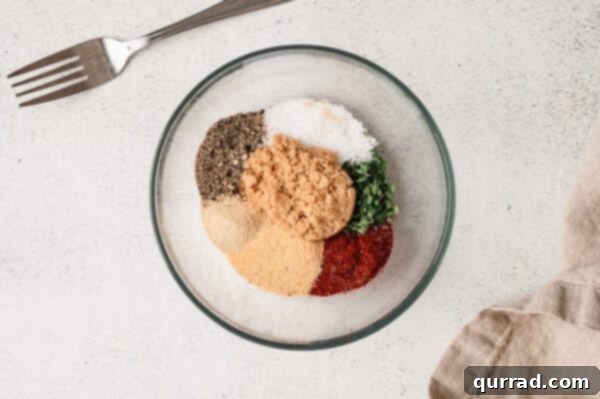 Sea salt, black pepper, rosemary, thyme, garlic powder, onion powder, smoked paprika, and dark brown sugar in a glass mixing bowl, ready to be whisked.