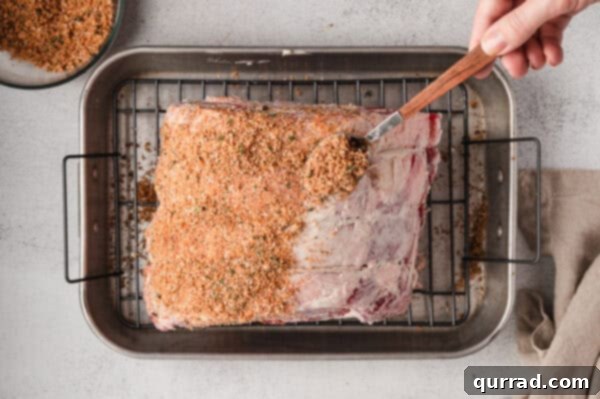 The homemade prime rib rub being generously sprinkled and rubbed over a large prime rib roast placed on a roasting tray, demonstrating the application process.