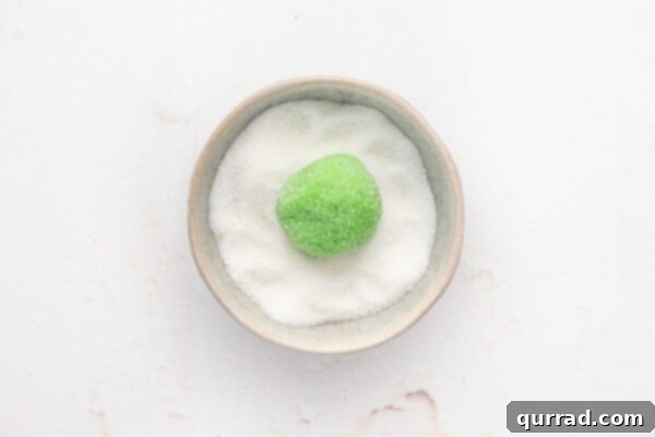 A ball of green sugar cookie dough in a bowl of sugar