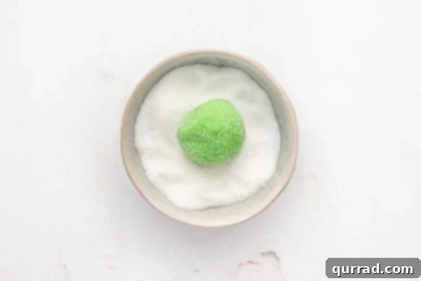 A ball of green sugar cookie dough in a bowl of sugar