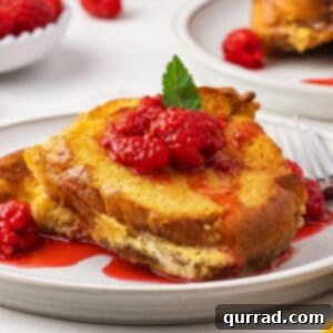 A serving of eggnog French toast casserole on a white plate with berry sauce
