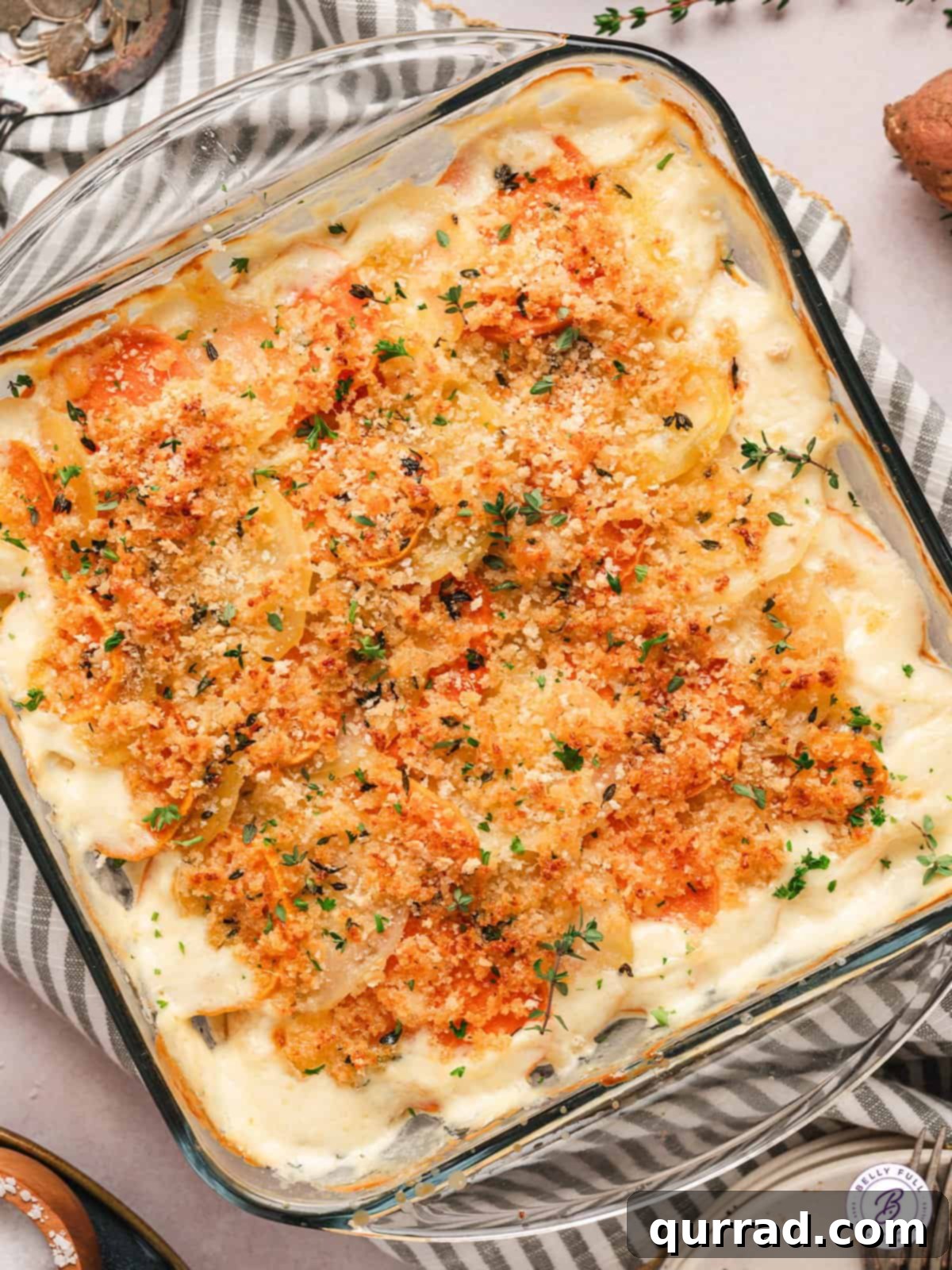 Yukon and Sweet Potato Gratin features layers of buttery Yukon gold potatoes and sweet garnet yams in a creamy sauce. Easy & impressive! Overhead view of a full baking dish of yukon gold and sweet potato gratin, golden and bubbling.