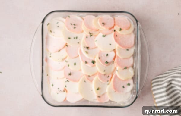 Harmonious Yukon and Sweet Potato Gratin 4 Cream sauce being poured over layered sweet potato and Yukon gold potato slices in a baking dish.