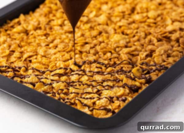 Crispy Cornflake Chocolate Bark 13 Melted chocolate being drizzled over cooled cornflake brittle on a baking sheet