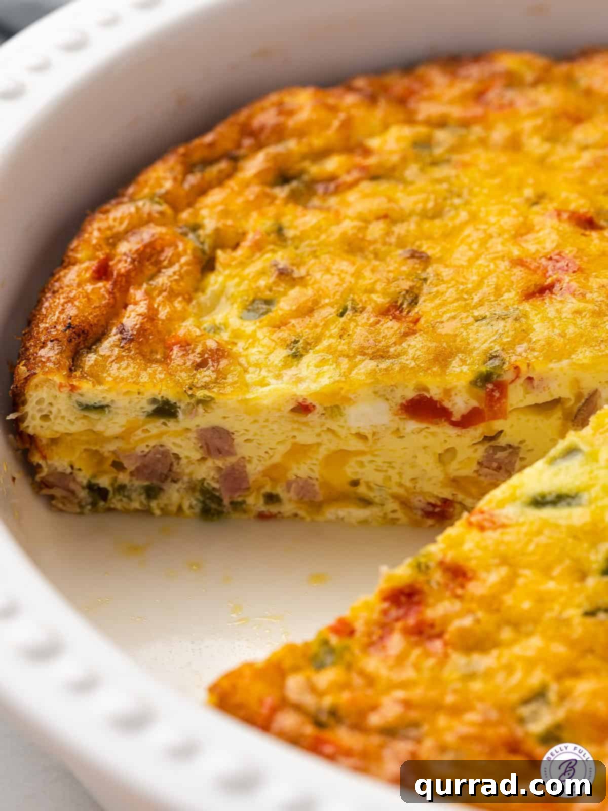 Made with diced peppers, onions, and ham, this Baked Denver Omelet is quick, easy, and great for serving a crowd. A baked Denver omelet with one slice already removed, showing its fluffy texture and filling.