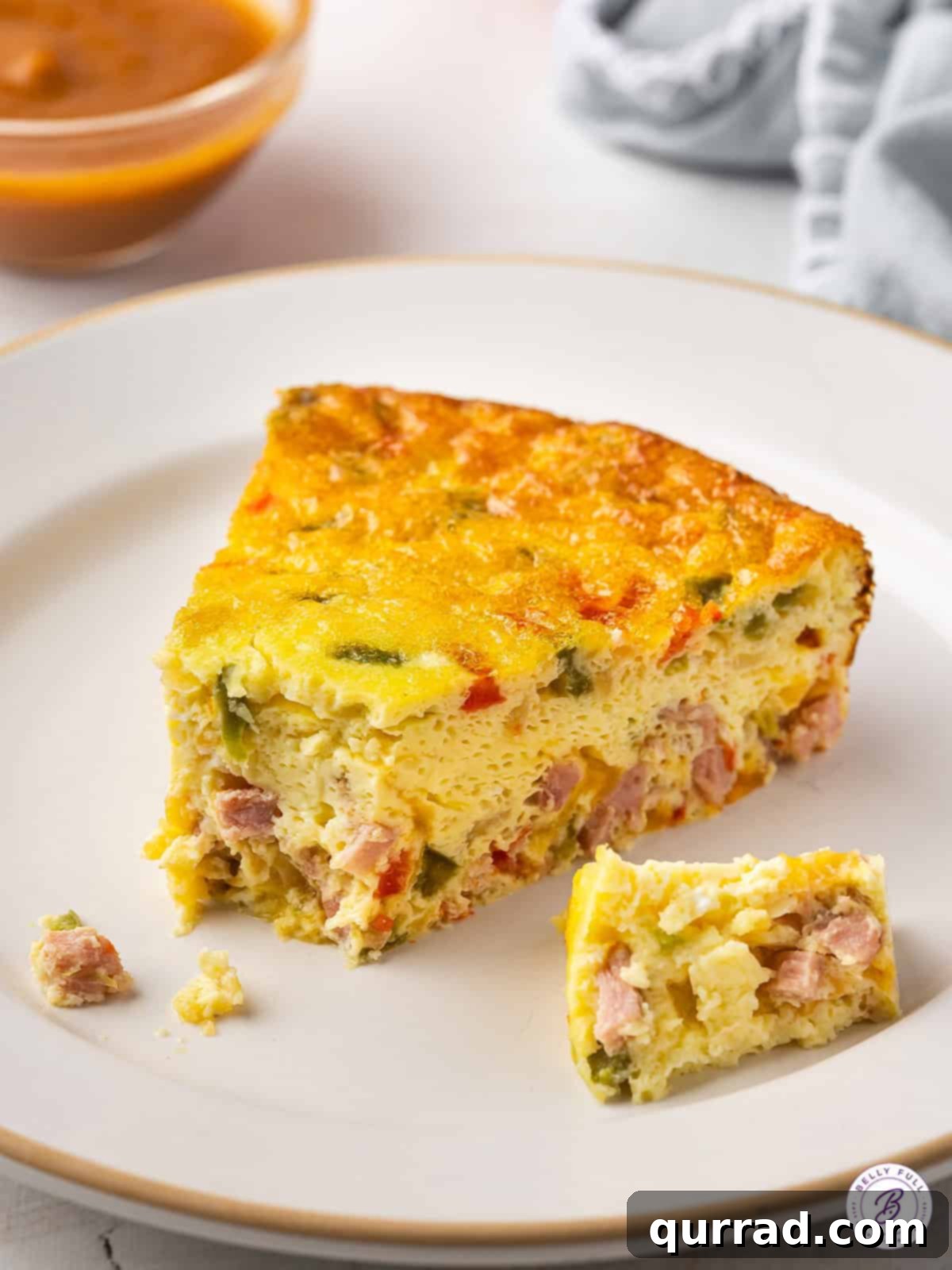 Made with diced peppers, onions, and ham, this Baked Denver Omelet is quick, easy, and great for serving a crowd. A plate featuring a slice of baked Denver omelet with a forkful taken, demonstrating its light and airy texture.