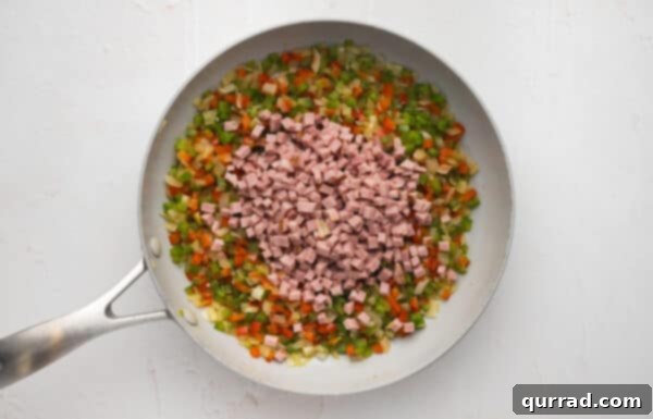 Diced ham added to a skillet with diced veggies, cooking together