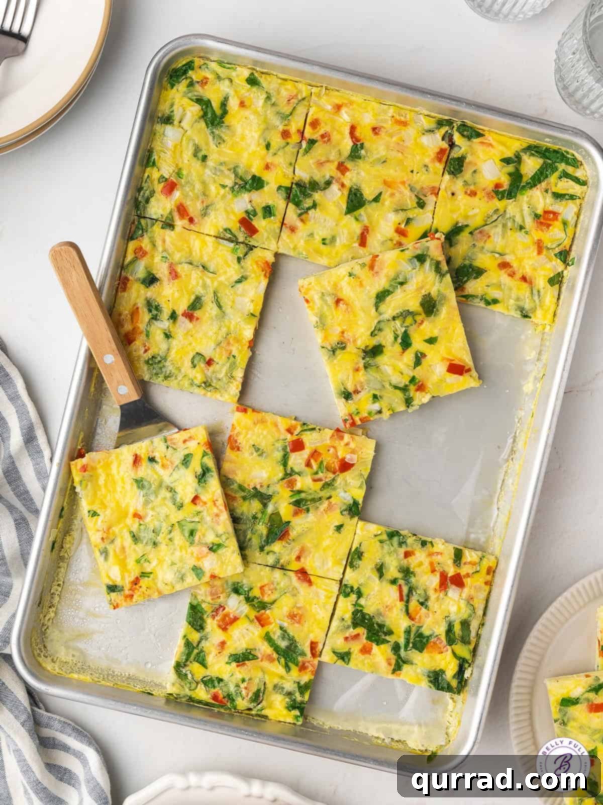 Eggs, cheese, and veggies make this Sheet Pan Egg Frittata an easy, filling breakfast that's perfect for serving a crowd. Overhead view of sheet pan frittata with various pieces sliced and missing