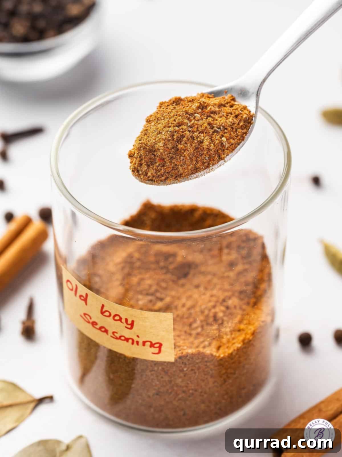 Perfectly Balanced: Homemade Old Bay Seasoning for Unforgettable Dishes. A measuring spoon filled with homemade Old Bay seasoning resting on a glass jar of the spice blend.