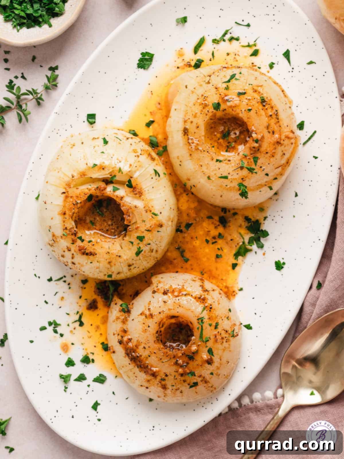 A sweet Vidalia onion is coated with butter, spices, and garlic and then baked in foil in this Onion Boil recipe. Simple & versatile! Overhead view of three baked onions on a white platter