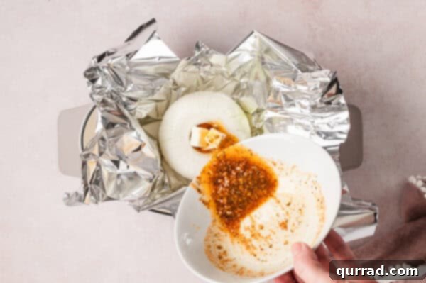Pouring melted butter with spices over a raw onion in foil