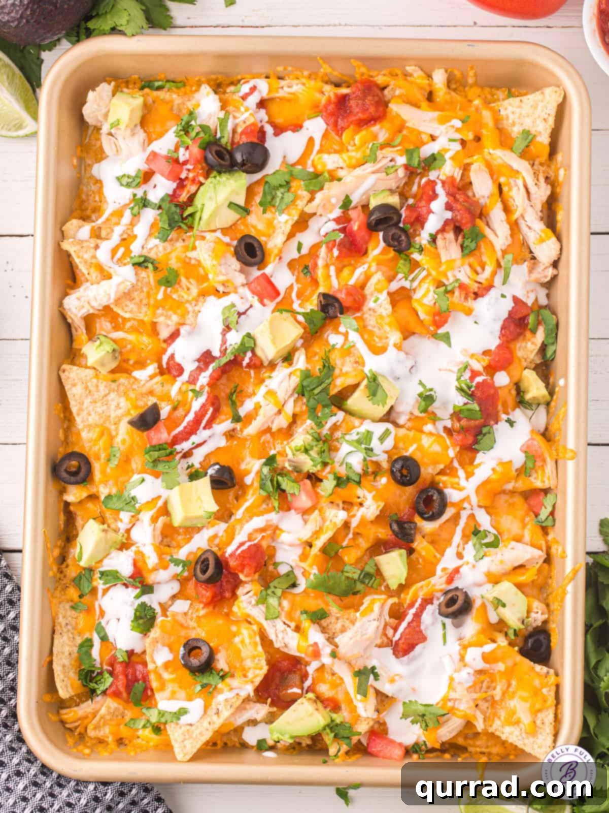 Layers of chips, cheese, and shredded chicken are baked and topped with all your favorite toppings in this Chicken Nachos recipe. Overhead view of a baking sheet of chicken nachos, loaded with toppings and ready to serve.