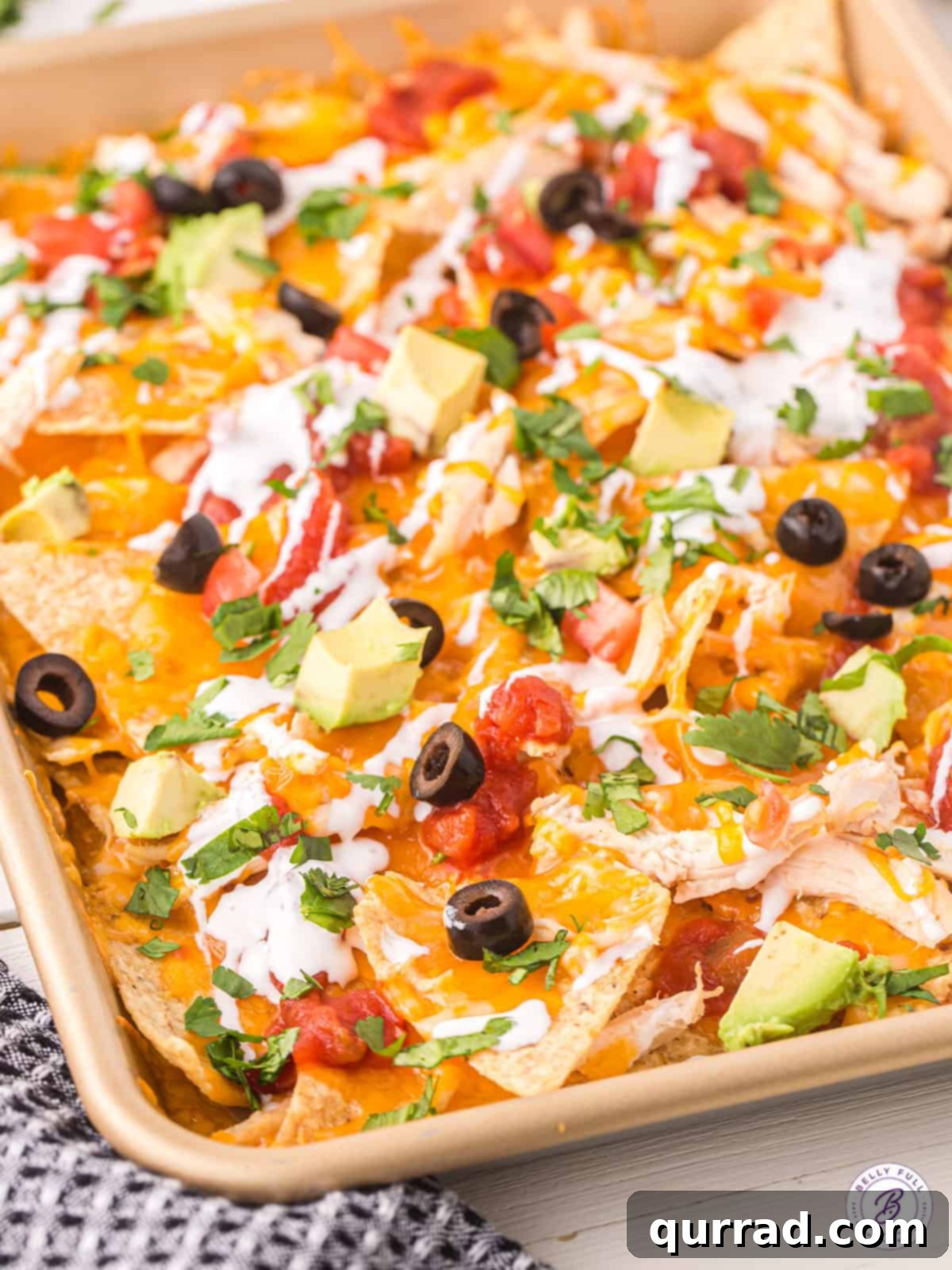 Layers of chips, cheese, and shredded chicken are baked and topped with all your favorite toppings in this Chicken Nachos recipe. A baking sheet of chicken nachos topped with olives, avocado, and green onions, fresh from the oven.