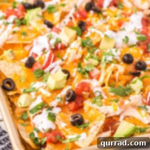 Loaded Chicken Nachos 2 A baking sheet of chicken nachos topped with olives, avocado, and green onions
