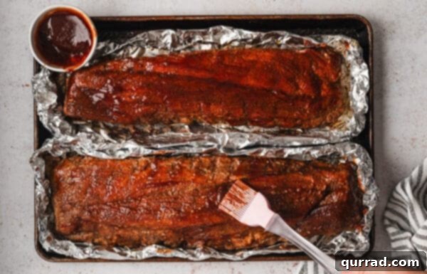 Fall-Off-The-Bone Baked Ribs 10 Brushing BBQ sauce on baked racks of ribs on foil