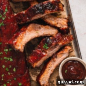 Fall-Off-The-Bone Baked Ribs 5 Overhead view of baked baby back ribs on a baking sheet with a side of BBQ sauce