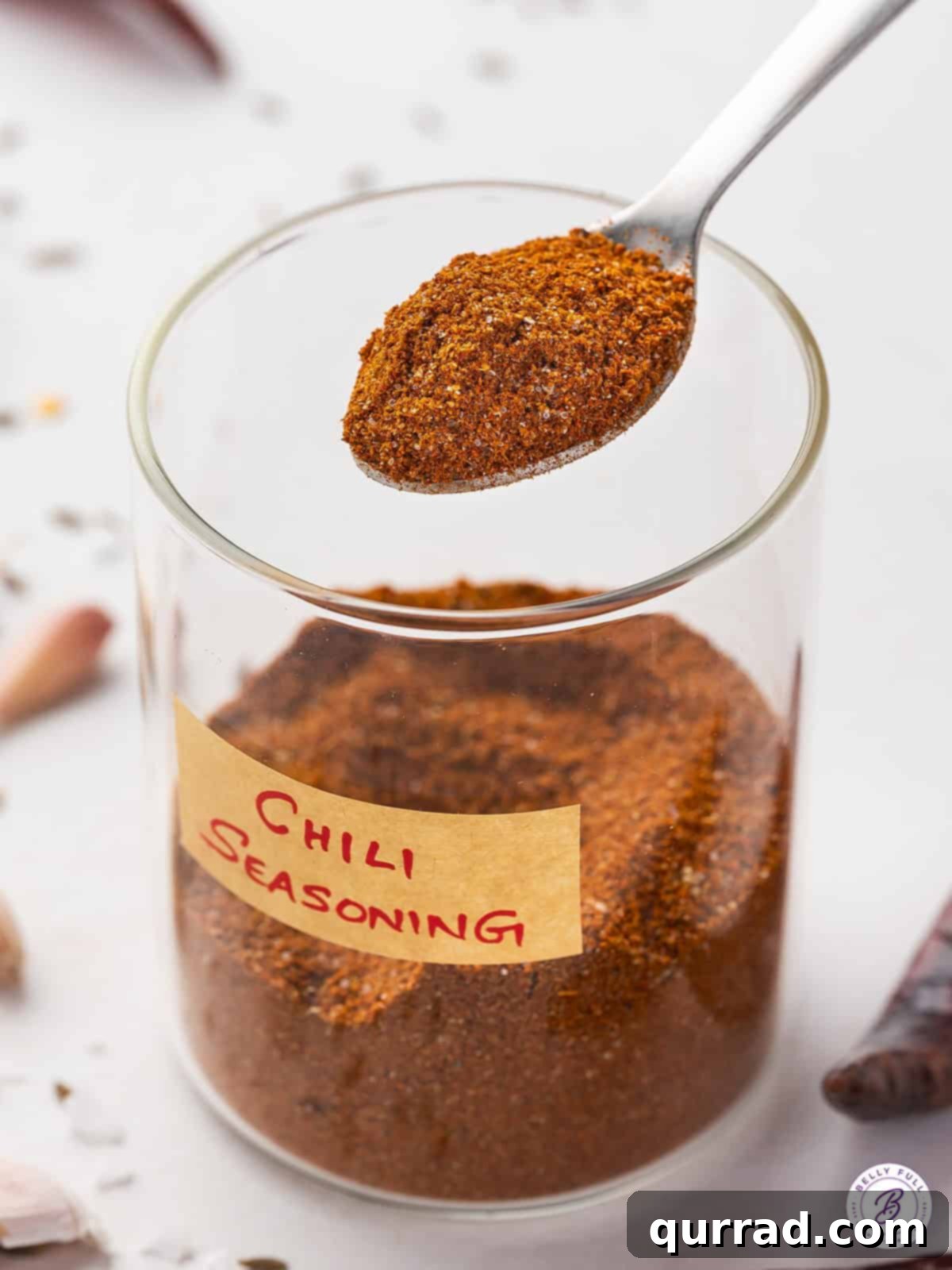A glass jar filled with homemade chili seasoning, with a wooden spoon resting over it, ready for use