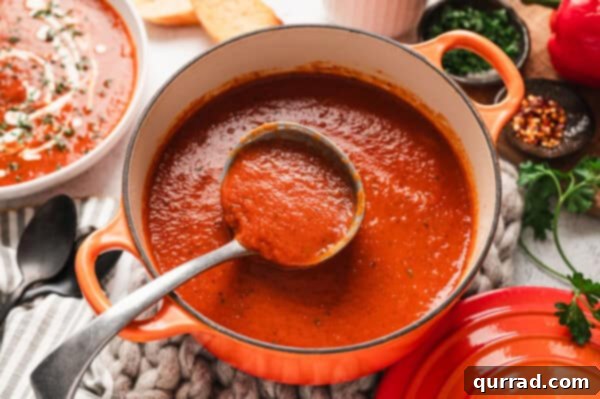 Roasted red pepper soup in a pot with a serving spoon.