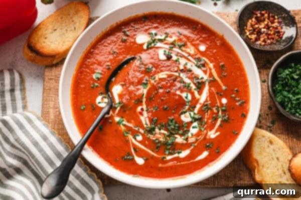 Overhead view of roasted red pepper soup, topped with cream and fresh parsley.