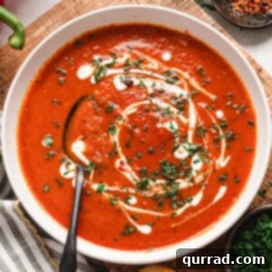 A bowl of roasted red pepper soup, topped with cream and fresh parsley, with a spoon
