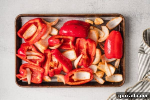 Overhead view of seasoned, quartered red bell pepper and sweet onion on a baking sheet.