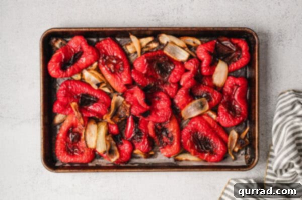 Overhead view of roasted, quartered red bell pepper and sweet onion on a baking sheet.