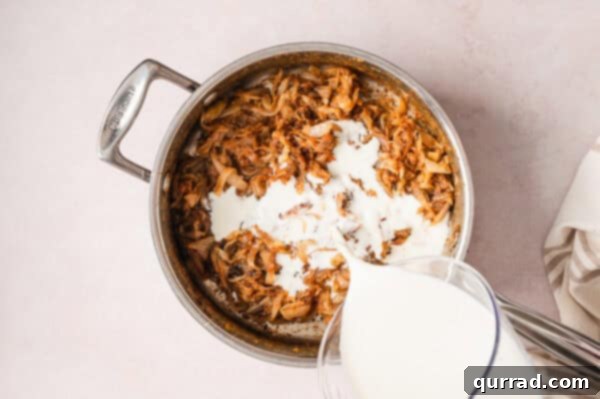 French Onion Macaroni Gratin 10 Whole milk being poured into caramelized onions in a pan.