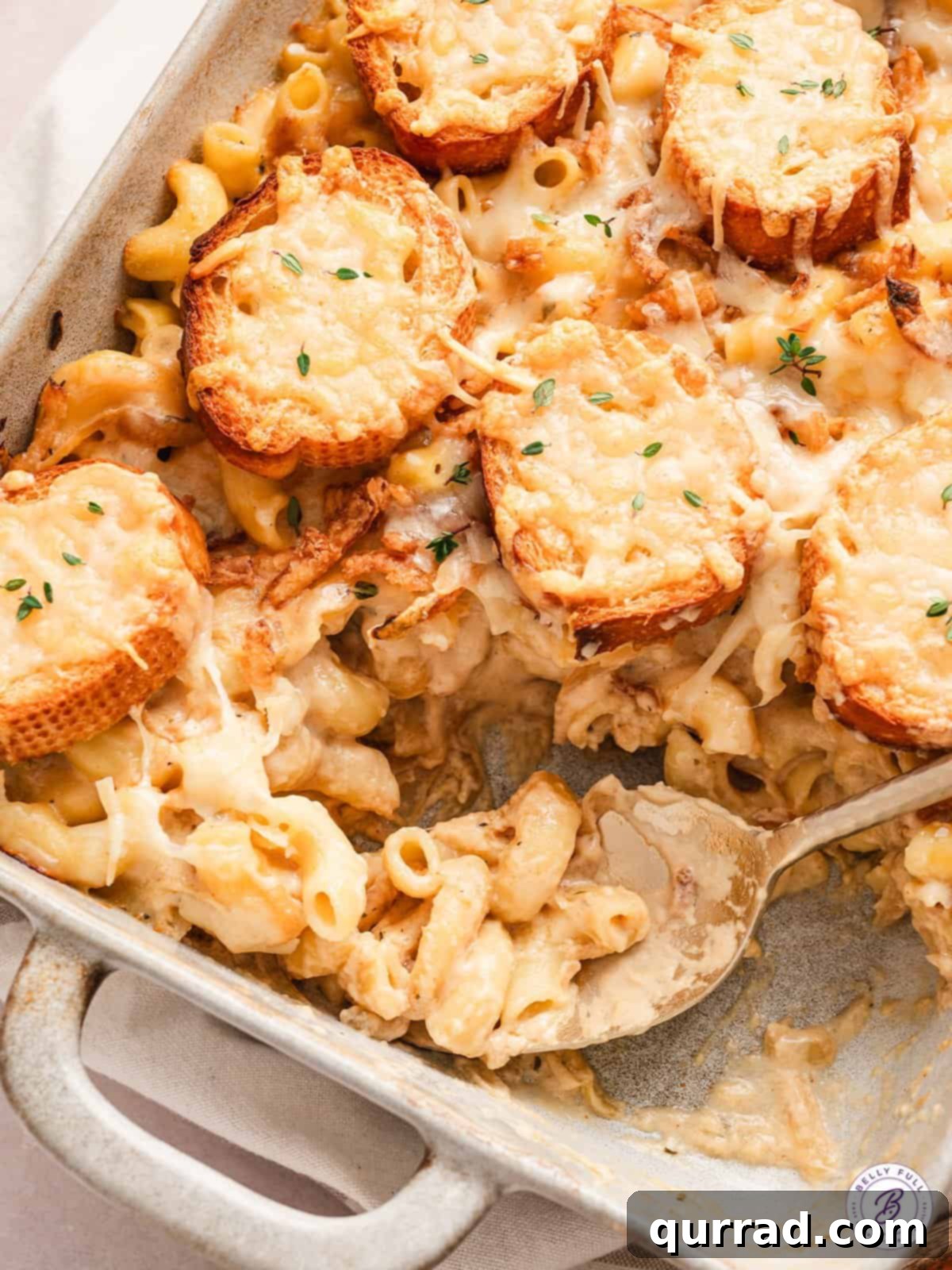 French Onion Macaroni Gratin 3 Overhead close up view of French onion mac and cheese in a baking dish, with a spoon scooping some out.