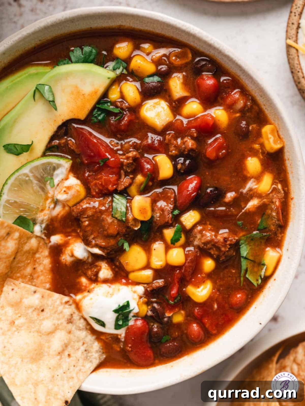 Seven Can Soup 2 Overhead view of a vibrant bowl of 7 can soup, garnished with creamy avocado slices, a wedge of fresh lime, and crispy tortilla chips, highlighting a quick and easy Tex-Mex dinner solution.