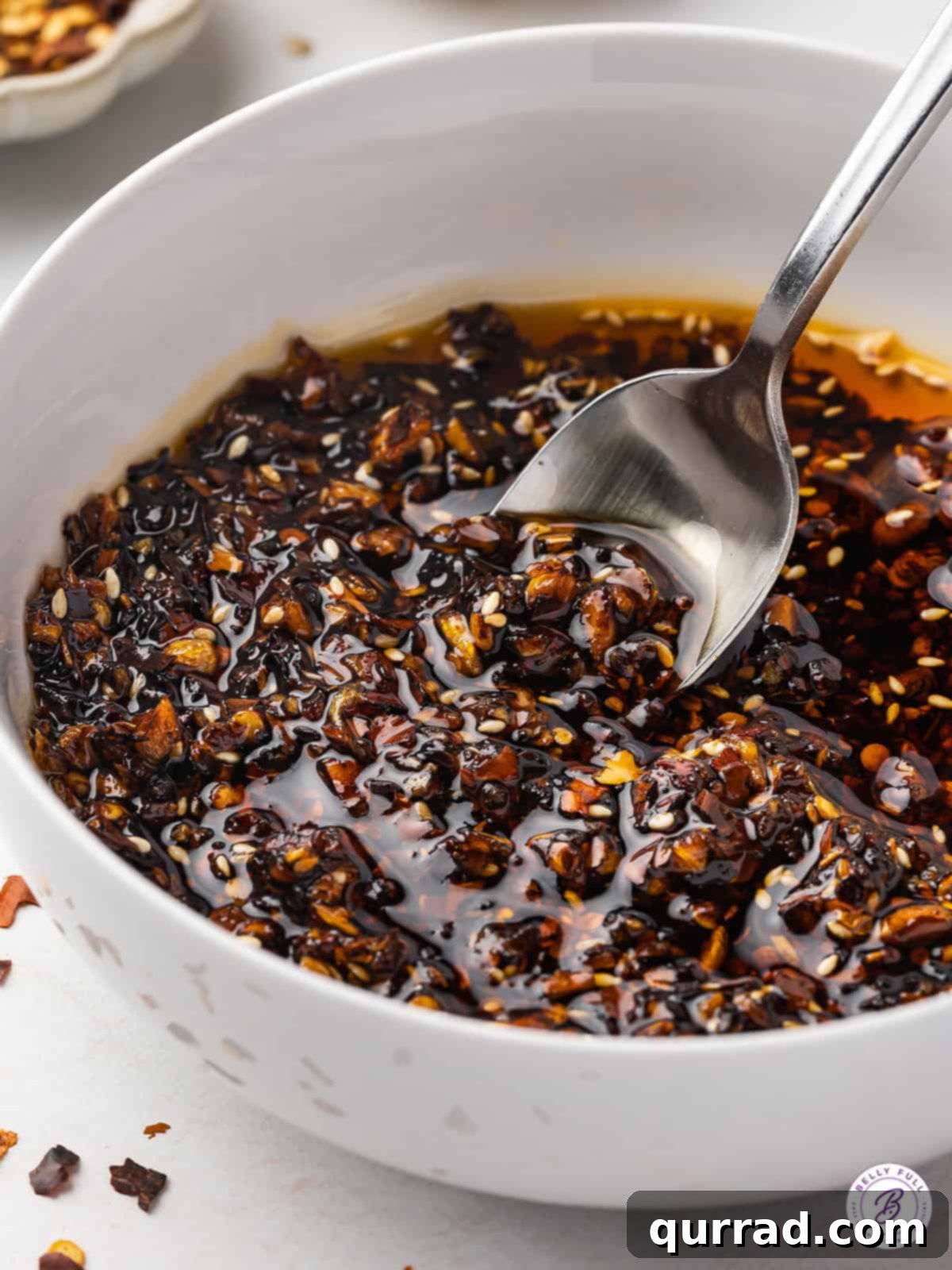 A spoon in a bowl of vibrant, homemade spicy chili crisp, showcasing its rich texture and inviting appeal.
