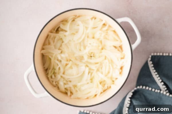 Thinly sliced onions cooking in melted butter in a large pot, starting to soften.