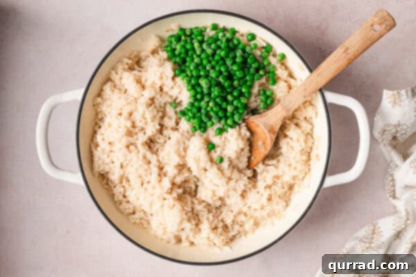 No-Stir Oven Risotto 8 A wooden spoon gently stirring bright green frozen peas into the creamy baked risotto.