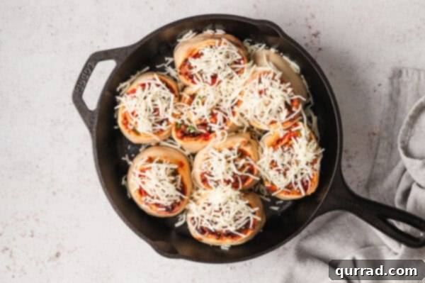 Mozzarella cheese on top of unbaked pizza rolls in a cast iron skillet