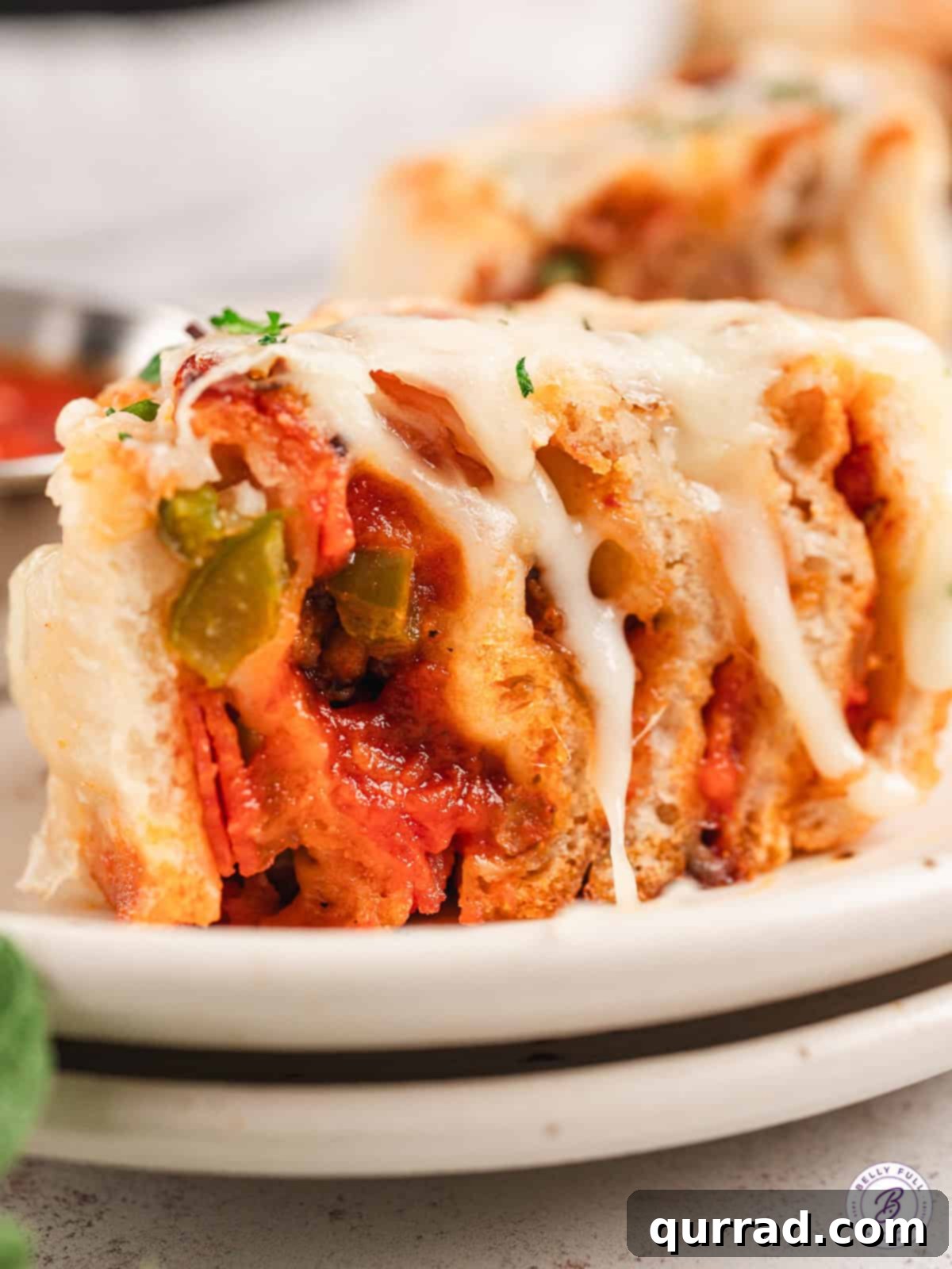 These Cheesy Supreme Pizza Rolls are loaded with pepperoni, sausage, peppers and lots of cheesy. A fun appetizer the entire family will love! A cheesy supreme pizza roll cut in half on a plate, showing the layers of filling.