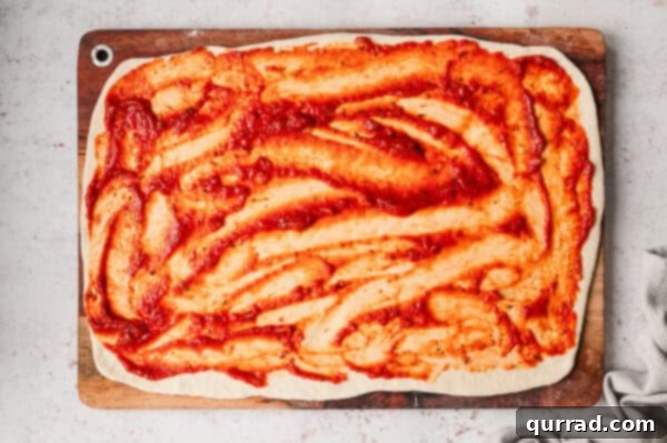 Marinara sauce spread on pizza dough