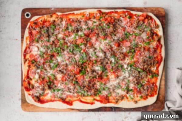 Pepperoni, sausage, and green bell peppers spread on pizza dough.