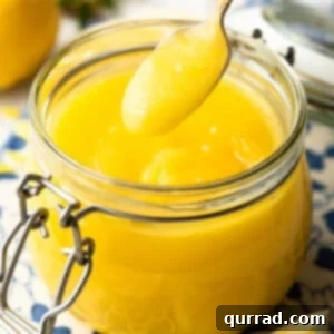 A spoon delicately scooping homemade lemon curd from a glass jar, highlighting its creamy texture.