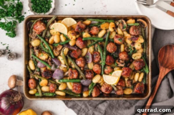 Gnocchi, sausage, and veggies on a sheet pan after roasting, garnished with fresh herbs and cheese
