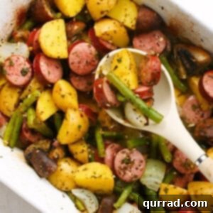 overhead baked sliced kielbasa and vegetables in casserole dish and serving spoon