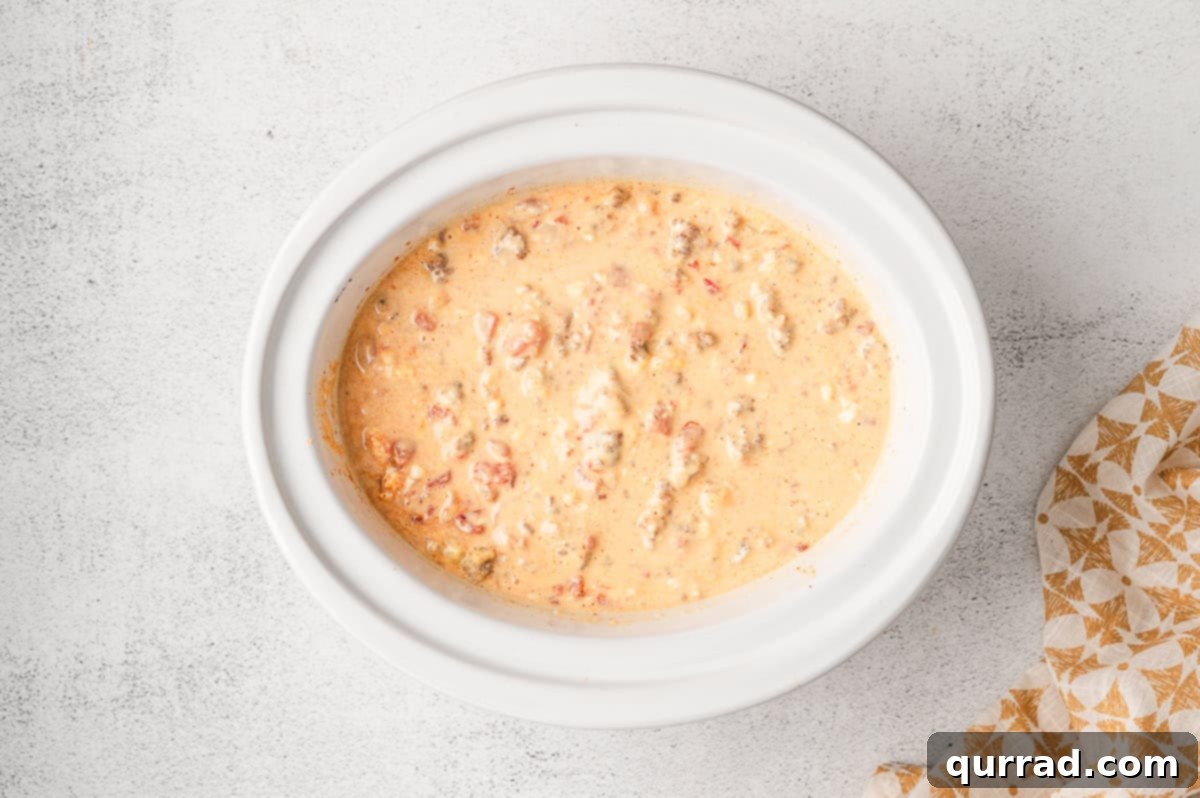 Overhead view of a crockpot bubbling with warm Rotel and sausage cheese dip, garnished with fresh cilantro.