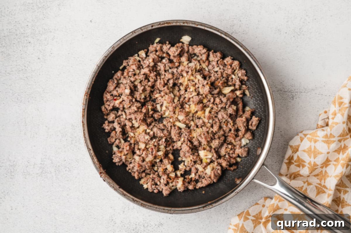 A pan filled with cooked crumbled sausage and softened onions, ready to be drained.