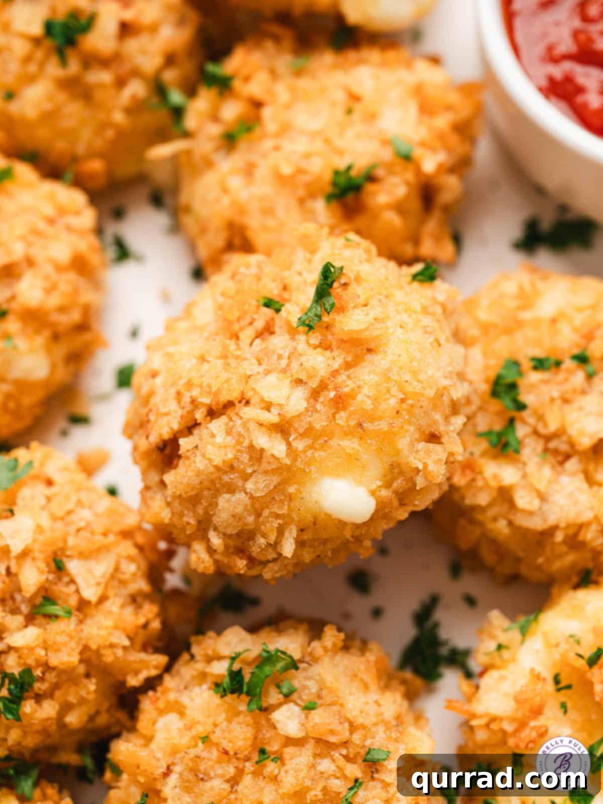 Experience cheesy bliss with Air Fried Babybel Cheese – coated in potato chips and air-fried to gooey, crispy perfection. The ideal quick appetizer or snack. Close up of air fried babybel cheese showcasing its golden-brown, crispy exterior and melted, gooey interior