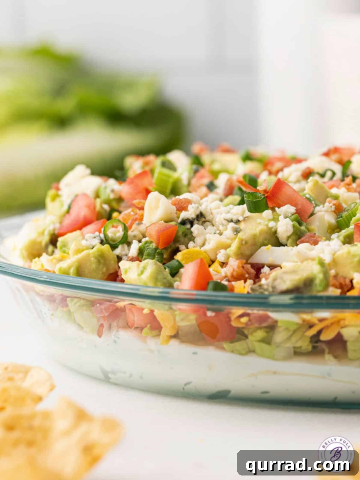 Layered Cobb Salad Dip: A feast for the eyes and the palate. Side view of a glass pie dish filled with layered Cobb Salad Dip, showcasing its vibrant ingredients.
