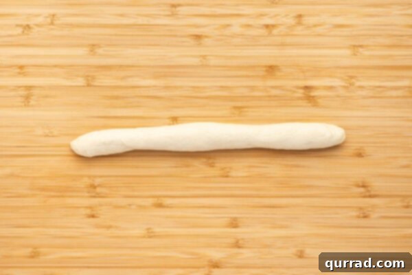 A thin log of dough being shaped into a rope before tying into a knot.
