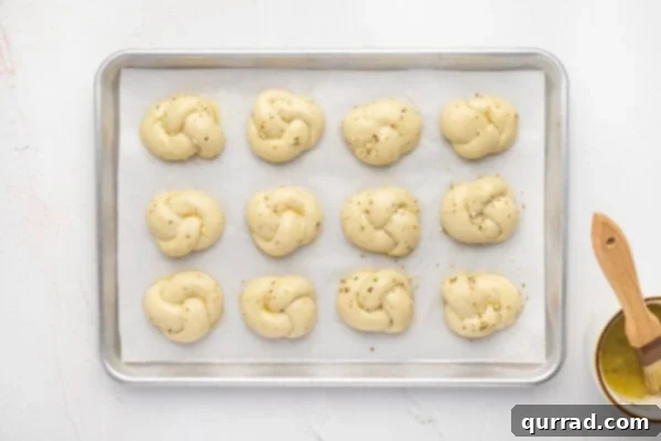 Shaped dough knots on a baking sheet after their second rise, looking puffy.