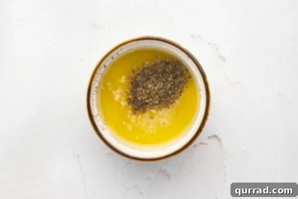 Melted butter infused with minced garlic and dried oregano in a small bowl.