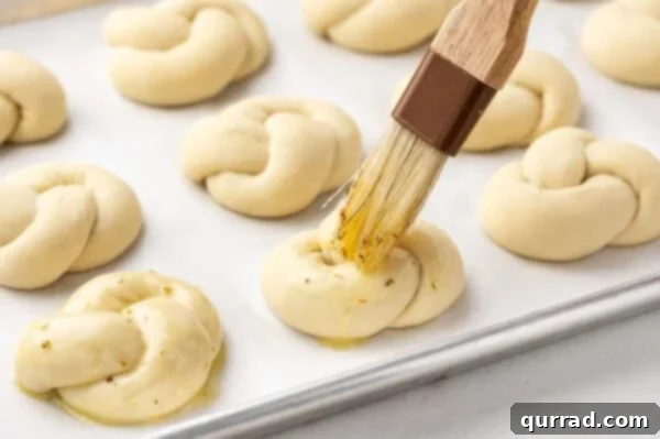 Garlic butter being brushed onto unbaked dough knots on a baking sheet.