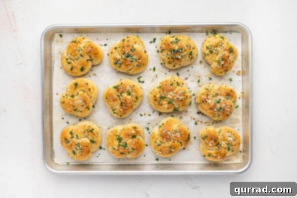 Overhead view of a tray of freshly baked garlic knots topped with Parmesan and parsley.