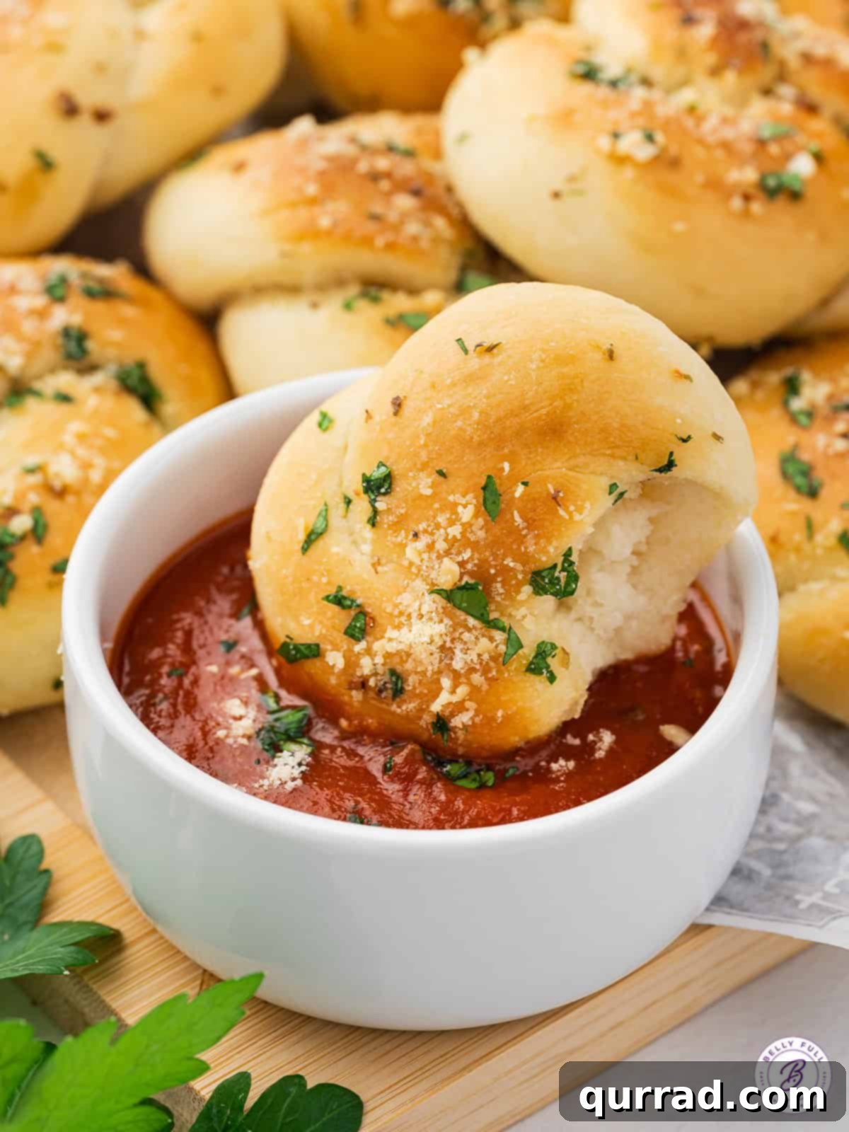 A tender homemade garlic knot being dipped into a small white dish of rich marinara sauce, highlighting its perfect texture and the delicious pairing.